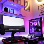 A sleek gaming setup featuring RGB lighting with a desktop, monitor, and smartphone in a vibrant room.